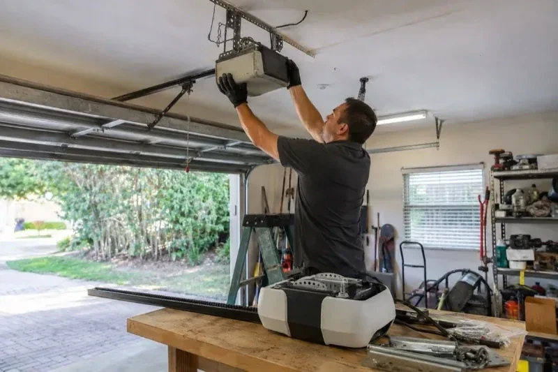 Person holding an overhead garage-door opener beside another opener and hardware on a workbench — Garage Door Opener Replacement, Kensal Park